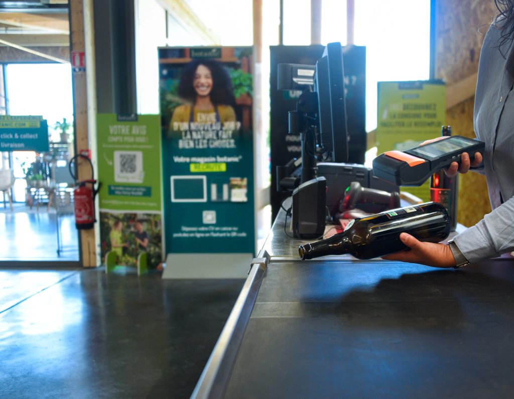 Hôte de caisse scannant avec le TCE une bouteille retournée pour réemploi